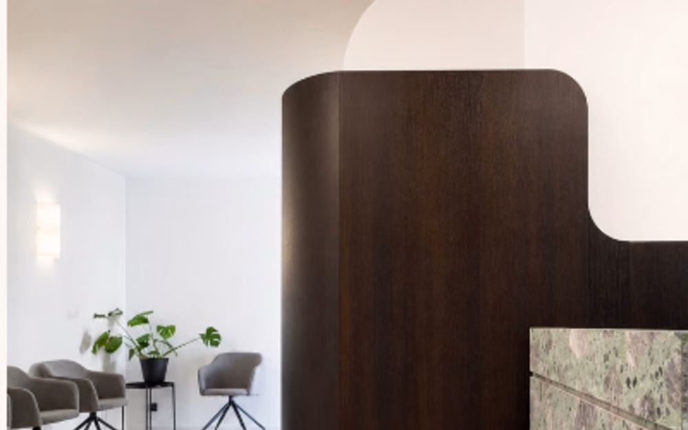 The reception at Site Botanique: a curved dark-timber desk beside a green marble counter, with seating along a pale wall