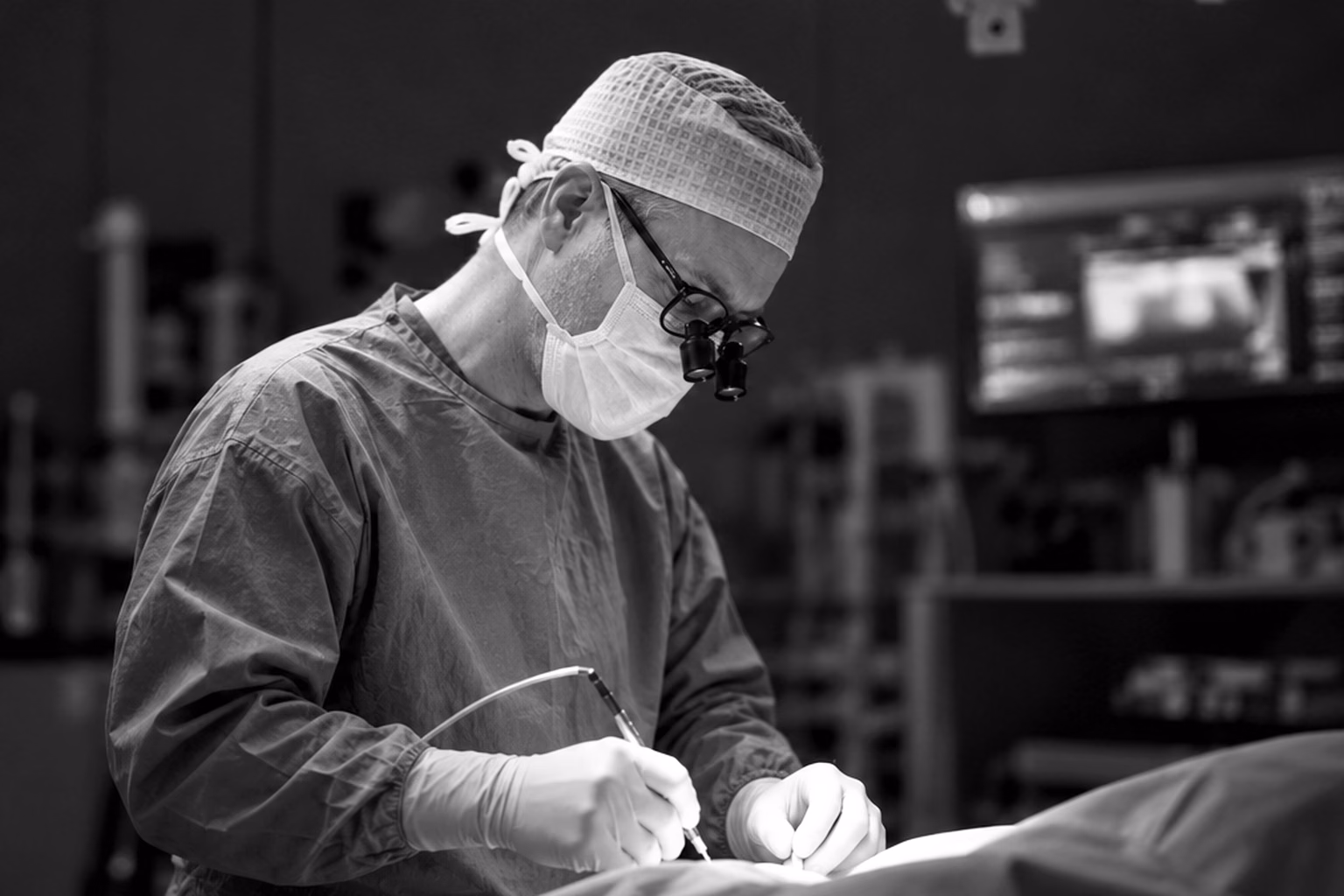 Le Dr Axel De Lange en train d’opérer, en blouse et loupes chirurgicales, photographié en noir et blanc