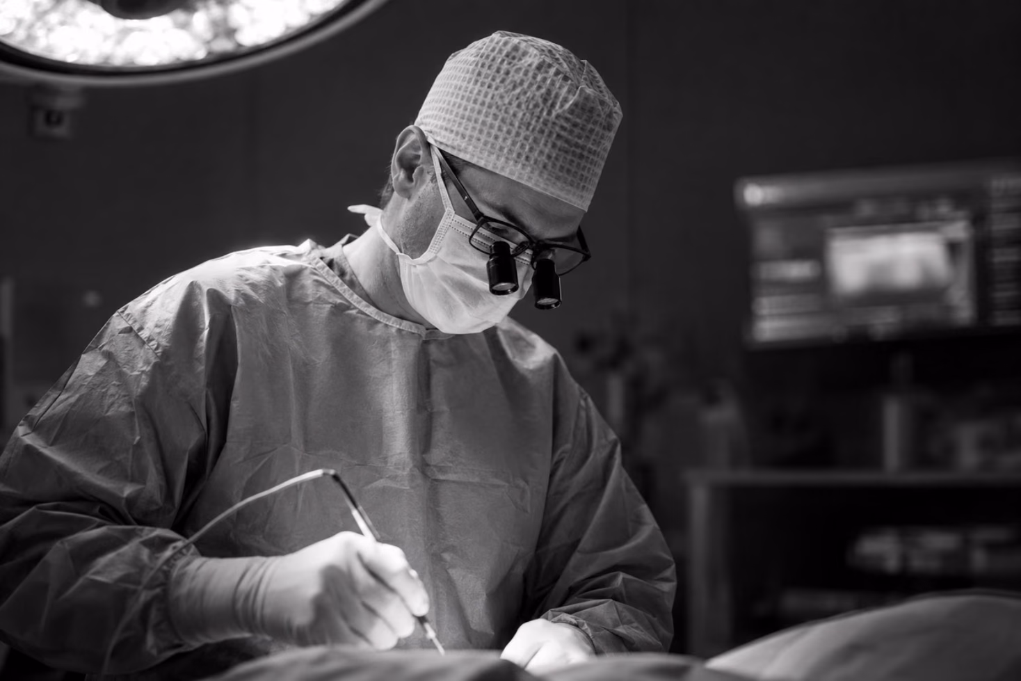 Le Dr Axel De Lange en train d’opérer, en blouse et gants, sous l’éclairage du bloc opératoire
